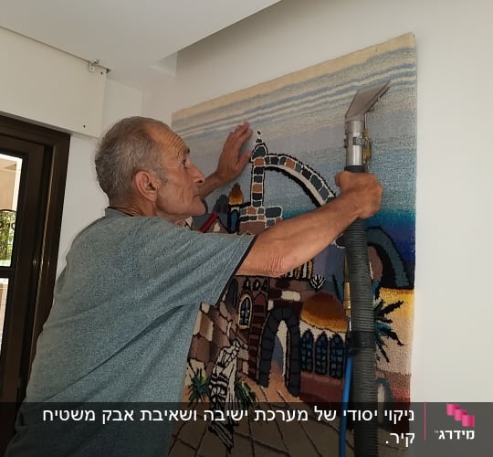 אדם מנקה שטיח תלוי עם שואב אבק